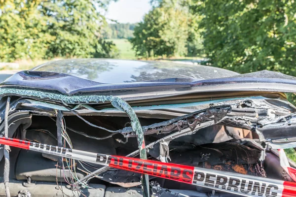 Burnt out car after a violent accident with police barrier tape in red and white with the German word for police barricade, Germany
