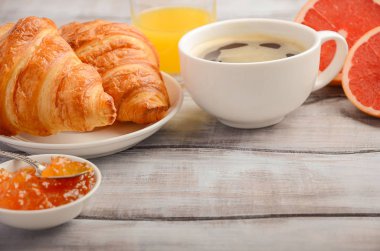 Rustik ahşap arka plan günü kahvaltıda kahve, reçel ve portakal suyu ile taze kruvasanlar.