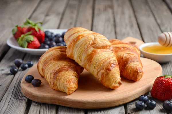 Fresh Croissants with fresh berries on rustic wooden background — Stock Photo, Image
