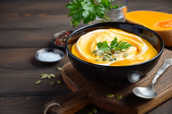 Kürbiscremesuppe mit Sahne und Kürbiskernen auf Holzgrund, selektiver Fokus — Stockfoto