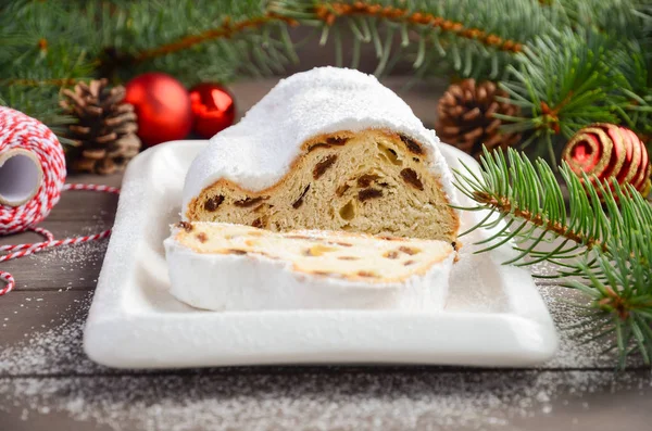 Christmas Stollen. Traditional German, European Festive Dessert on Old Wooden Table. Holiday Concept Decorated with Fir Branches and Cones.