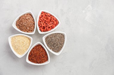 Gri beton zemin üzerine beyaz kase superfoods seçimi. Quinoa, chia, goji berry ve keten tohumu. Üstten Görünüm, düz yatıyordu, kopya alanı.