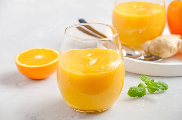 Fresh healthy smoothie with persimmon, orange and ginger on gray concrete background. Selective focus.