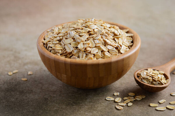Овсяные хлопья в деревянной миске и деревянной ложке на светло-коричневом фоне, избирательный фокус
.