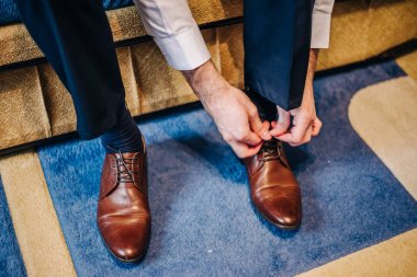 damat kanepede oturuyor, ellerini düğün gününde kahverengi deri ayakkabı bağlama