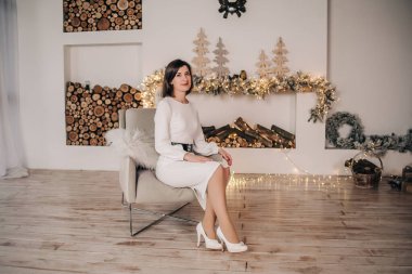 Beyaz elbiseli bir manken, Noel iç dekorasyonu olan bir odada koltukta oturur.