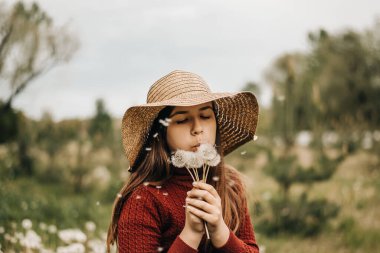 Hasır şapkalı kız, karahindiba desenli yatay çekimde uçuyor.