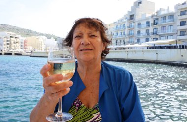 Elinde bir kadeh beyaz şarap tutan yaşlı bir kadın. Açık havada portre