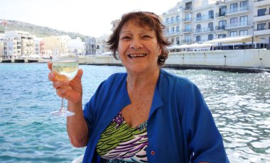 Elinde bir kadeh beyaz şarap tutan yaşlı bir kadın. Açık havada portre