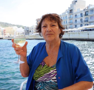 Yaşlı kadın elinde bir kadeh beyaz şarap tutuyor.