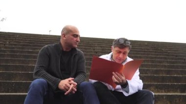 Doktor dışarıda oturup bir hastayla konuşan ve sonuçları açıklayan bir sağlık raporunu inceliyor.