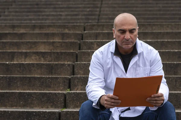 Absorbed medical doctor or dentist sitting on outdoor stairs and reading a clinical study report