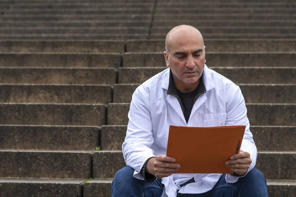 Absorbed medical doctor or dentist sitting on outdoor stairs and reading a clinical study report