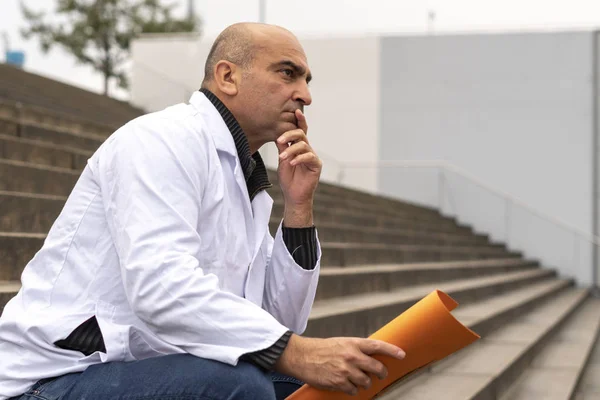 Absorbed medical doctor or dentist sitting on outdoor stairs holding a clinical study report