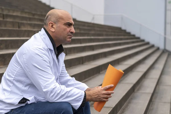 Absorbed medical doctor or dentist sitting on outdoor stairs holding a clinical study report