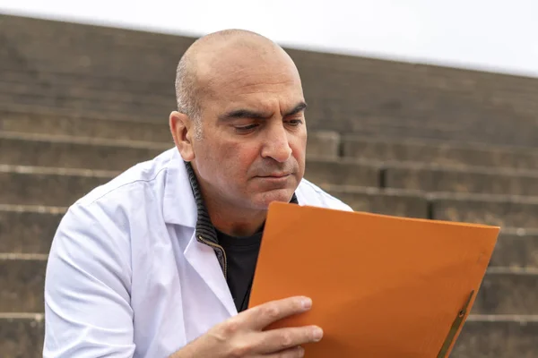 Absorbed medical doctor or dentist sitting on outdoor stairs and reading a clinical study report