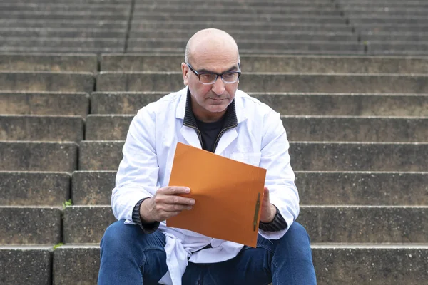 Absorbed medical doctor or dentist sitting on outdoor stairs and reading a clinical study report