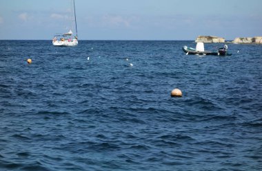 Maltese mavi denizinde demirli yelkenli ve kauçuk tekne
