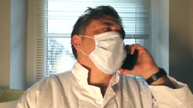 Cerrahi maske takan endişeli doktor telefonla konuşuyor.
