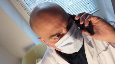 Cerrahi maske takan endişeli doktor telefonda endişe verici haberler alıyor.