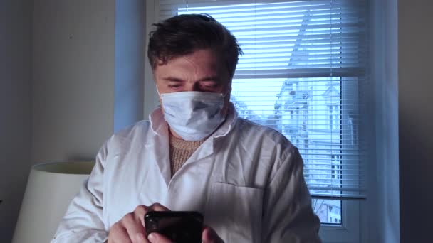 Bezorgde Arts Draagt Een Chirurgisch Masker Typt Zijn Mobiele Telefoon — Stockvideo