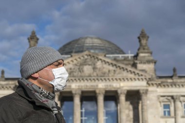 Şehrin tecridi sırasında Berlin Reichstag binasının önünde tek başına poz veren yetişkin bir adam yüzüne koruyucu maske takıyor.