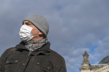 Şehrin tecridi sırasında Berlin Reichstag binasının önünde tek başına poz veren yetişkin bir adam yüzüne koruyucu maske takıyor.