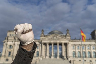 Elindeki lateks eldivenle sol yumruğunu Berlin 'deki Alman Bundestag' ına gösteriyor. Seçici odak
