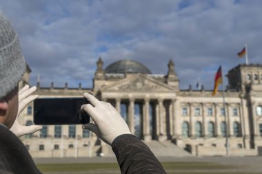 Berlin Bundestag binasının akıllı telefonuyla fotoğrafını çeken adamın elleri tıbbi koruyucu eldivenlerle kaplı.