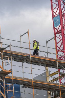 Berlin, Almanya - 31 Mart 2020: Tanımlanamayan inşaat işçisi cep telefonuyla konuşuyor iskele üzerinde ileri geri yürüyor
