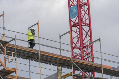 Berlin, Almanya - 31 Mart 2020: Tanımlanamayan inşaat işçisi cep telefonuyla konuşuyor iskele üzerinde ileri geri yürüyor
