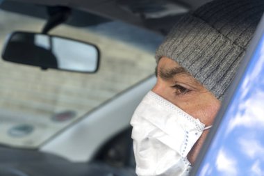 Direksiyondaki adam burnunu ve ağzını korumak için yüzünü tıbbi maskeyle kapatıyor.