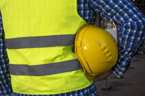 一名建筑工人身穿黄色防弹背心 腋下戴着黄色头盔的剪影 — 图库照片