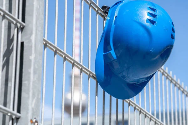 Occupational safety and safety gear. Blue hard hat hanging on scaffolding. Focus on foreground. On background out of focused Berlin television tower, Germany landmark