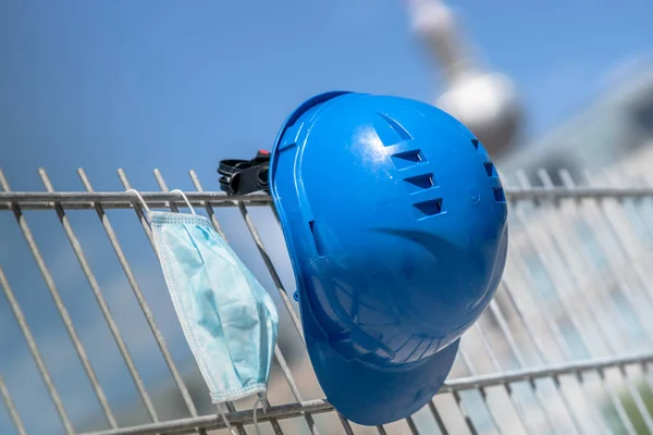 Occupational safety and protection against adverse conditions at work. Blue hard hat and protective surgical mask hanging on scaffolding. On background out of focused Berlin television tower