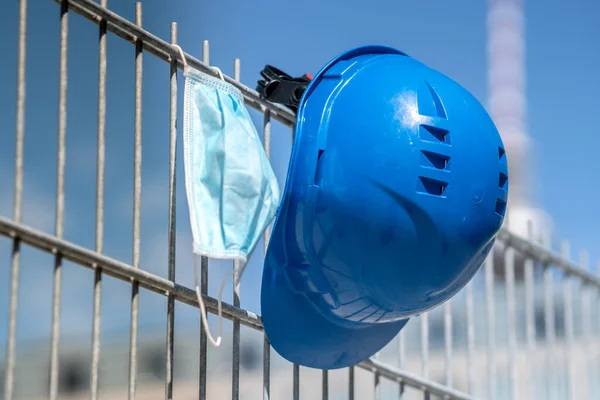 Occupational safety and protection against adverse conditions at work. Blue hard hat and protective surgical mask hanging on scaffolding. On background out of focused Berlin television tower