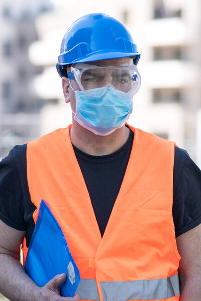 Engineering during COVID-19 (Coronavirus SARS-CoV-2) outbreak. Occupational safety and health and protection against adverse conditions at work. Construction worker with hardhat, vest goggles and mask