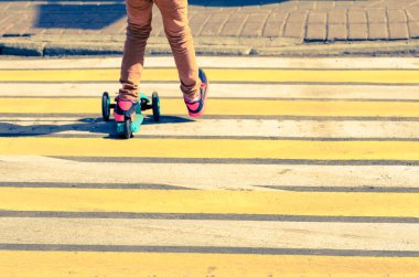 Tekmeleyen scooter 'daki çocuk yoldan geçen zebranın üzerinde.