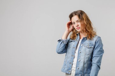 Young girl with long flowing hair in a denim looks thoughtfully at the camera and touches her hair. Half-length portrait