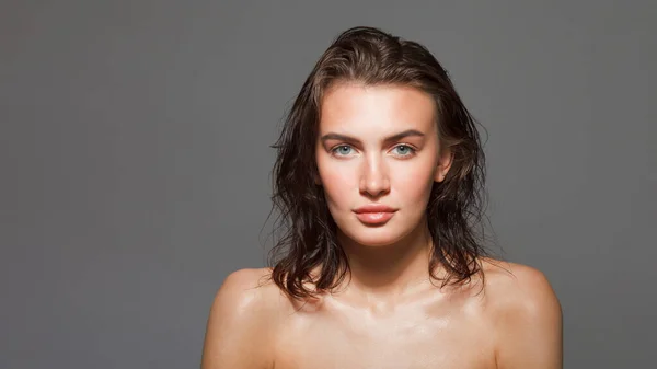 Young candid girl with long wet hair and bare shoulders looks at the camera. Close up portrait against dark background
