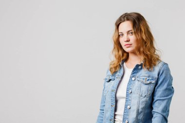 Candid young girl with long flowing hair in a denim looks calmly at the camera. Half-length portrait on white background