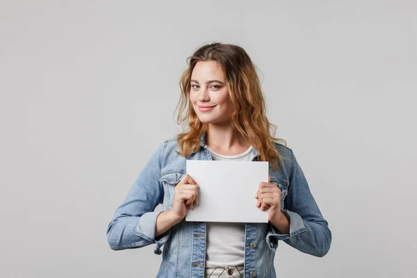 Young sixteen year old girl girl with flowing hair in a denim smiles slyly, looks at the camera and holds a mock up card