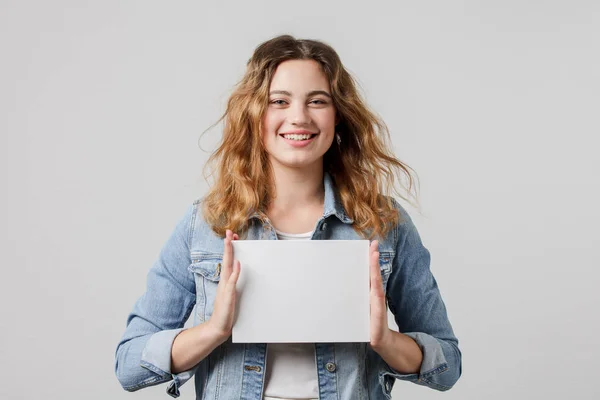 Candid young girl with long hair holds mock up card with hands, looks and smiles at the camera