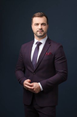 Koyu mavi arka planda poz veren zarif takım elbiseli başarılı bir adam..