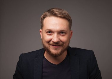 Karanlık arka planda gülümseyen yakışıklı adam kameraya bakıyor..