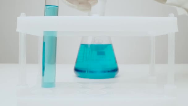 La cámara se acerca a un frasco de vidrio con líquido azul pasado un contener — Vídeos de Stock