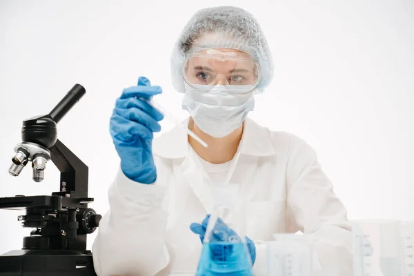 Koruyucu maskeli kadın çalışan laboratuarda reaksiyonlarla koronavirüs testi yapıyor.