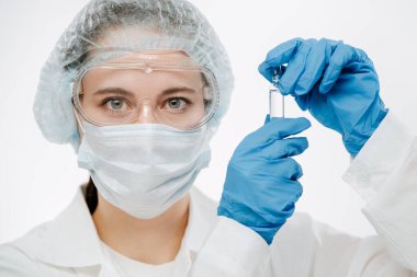 Maskeli genç bilim adamı klinikte koronavirüs ilacı tutuyor.