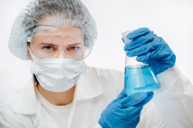 Koronavirüs testi yapmak için koruyucu maskeli bir doktor elinde şişe tutuyor.