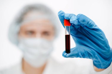 Mavi eldivenli genç laboratuvar asistanı klinikte koronavirüslü kan tutuyor.